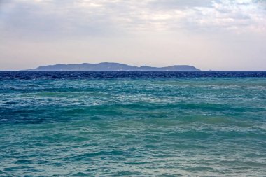 Güneşin doğuşunda ihale bulutlarının altında lacivert ve turkuaz deniz dalgaları ile ufukta Korfu adasının gizemli silueti. Yunanistan 'daki Erikousa adadan görünüm