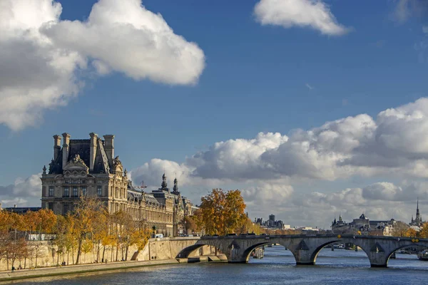 Lions Gate vintage building (Porte des Lions) with autumn trees on the bank of the river Seine with Pont Royal bridge under beautiful blue sky with clouds in Paris, France