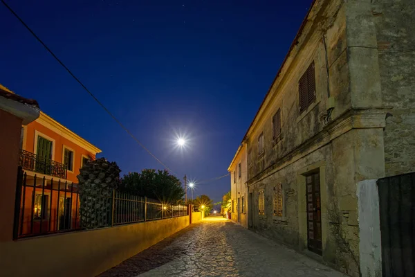 Perspective view with ancient village houses with full moon in starry blue sky at night on Erikousa island, Greece