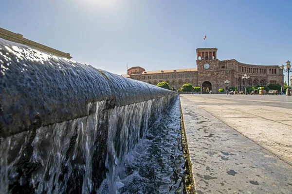 Extremely low wide angle perspective view of water overflowing the edge of the pool of famous Singing Fountains on Republic Square in Yerevan, Armenia with Government building on blurred background