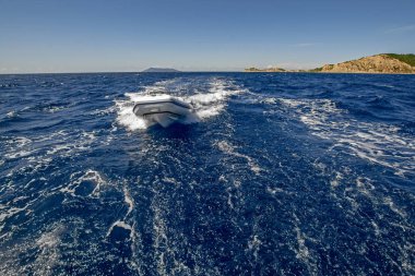 Motorkauçuk tekne arka planda gizemli ada ile mavi denizde yüksek hızda yelken
