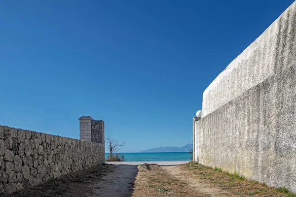 Abstract perspective scene with white wall, stone fence and turquoise sea under the blue sky. Clean architectural geometric elements design concept in white and blue
