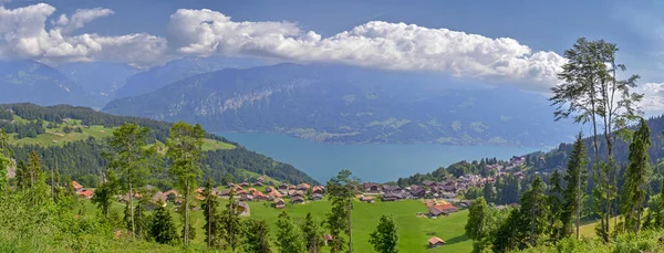 晴れた日にスイスアルプスの森林に覆われた山々の斜面にタイル屋根とトゥーン湖 Thunersee と伝統的な小屋と美しいパノラマ ビーテンベルク スイス — ストック写真