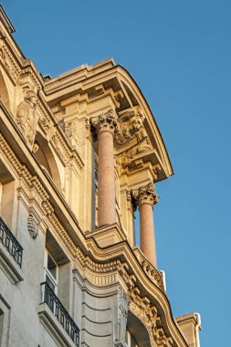 Paris, Fransa 'nın orta kesimindeki tarihi binalardan birinin dekoratif unsurların ve sütunların alçak açılı görüntüsü gün batımıyla aydınlanıyor.