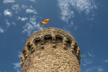 İspanya 'nın Tossa de Mar kentindeki Vila Vela Kalesi' nin mavi bulutlu arka planında Katalonya bayrağıyla alçak açılı ünlü kulesinin görüntüsü