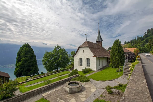 Christian place of worship and religion. Evangelical Reformed parish of  Beatenberg, Switzerland under the cloudy sky in Swiss Alps and Thun lake (Thunersee) on background