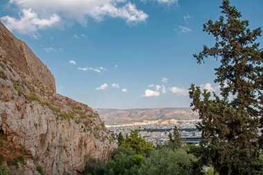Arka planda Akropolis 'in güneybatı taş duvarının ve mavi gökyüzü ve Atina' nın altındaki yeşil ağaçların manzarası, Yunanistan