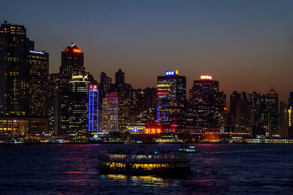 Hong Kong, China - February 20, 2014: Beautiful skyline cityscape downtown skyscrapers over Victoria Harbour in the evening with illuminated tourist ferry boats on sunset