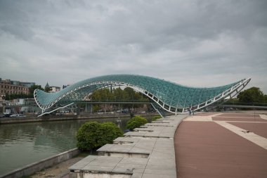 Tiflis, Gürcistan - 17 Mart 2018: Tiflis, Gürcistan şehir merkezindeki Kura Nehri 'nin üzerindeki yay şeklinde yaya köprüsü, çelik ve cam yapı