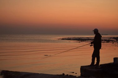 Gün batımında elinde dönen balıkçı silüetinin yanında.