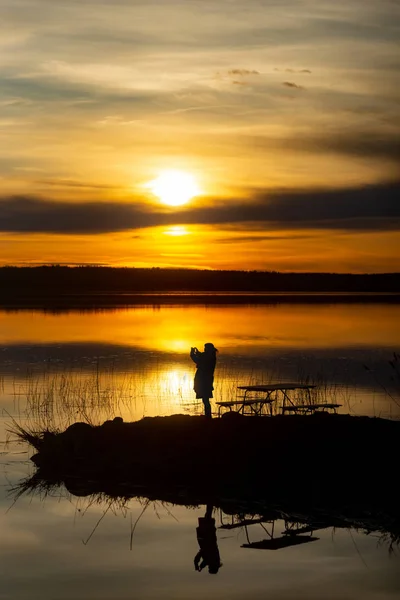 妇女用手机拍摄日落照片的剪影 在水中反射 — 图库照片