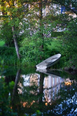 Sarı konağın önünde küçük beyaz sandal, bir nehrin sakin suyunda yansımaları ile