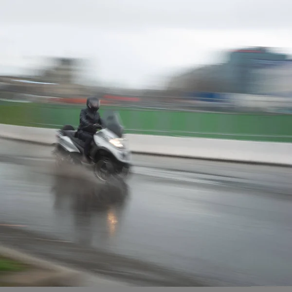 Man on three wheel motorcycle in blurred motion in heavy rain