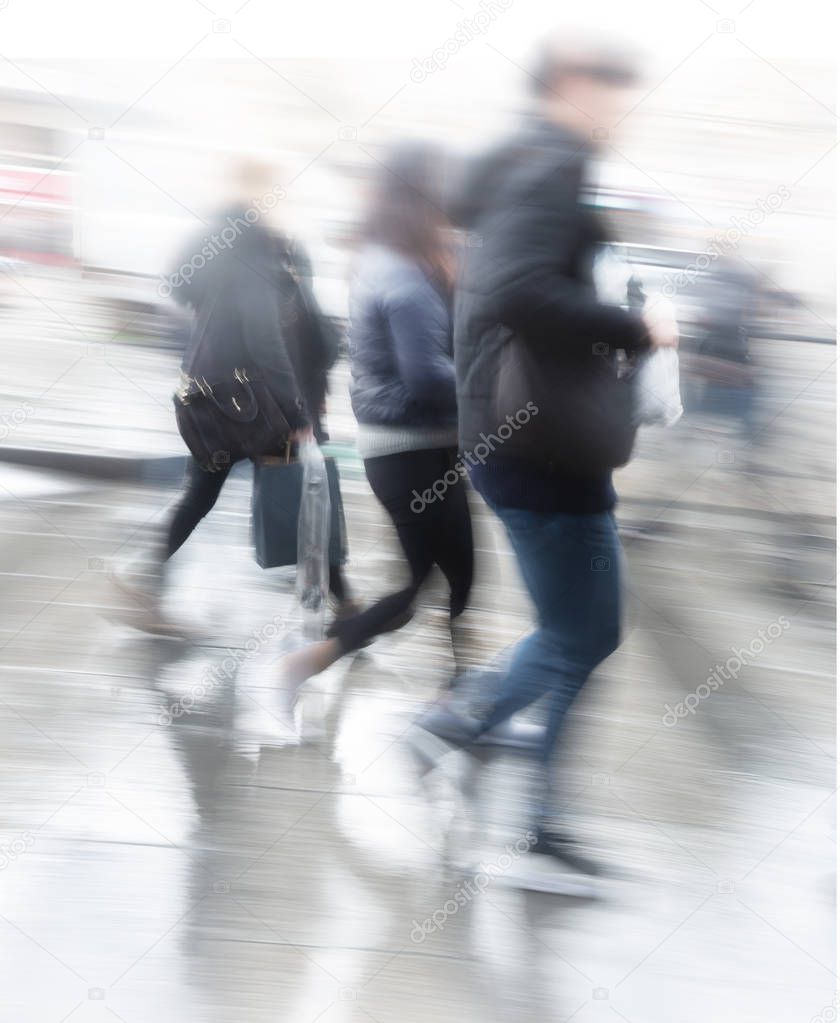 People in blurred motion rushing over pedestrian crossing on rainy day