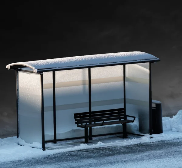 冬のバス停の空のベンチ 背景に暗い空と低い太陽からのいくつかの薄暗い光 — ストック写真