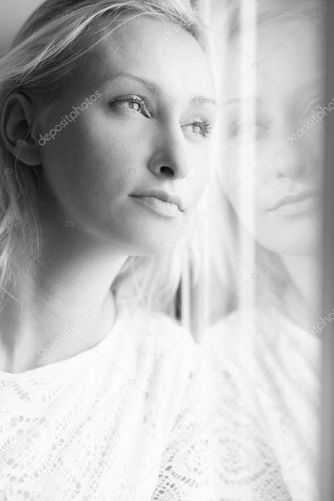 black and white shot of beautiful blonde woman leaning on window