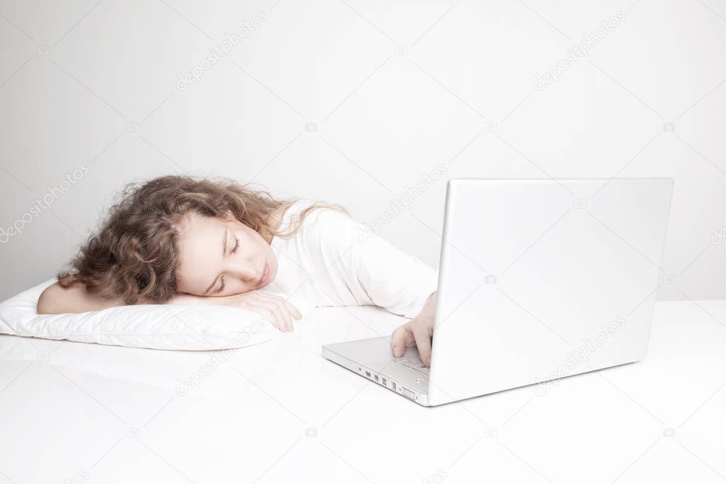 overworked redhead woman sleeping at workplace while working with laptop in front of white wall 
