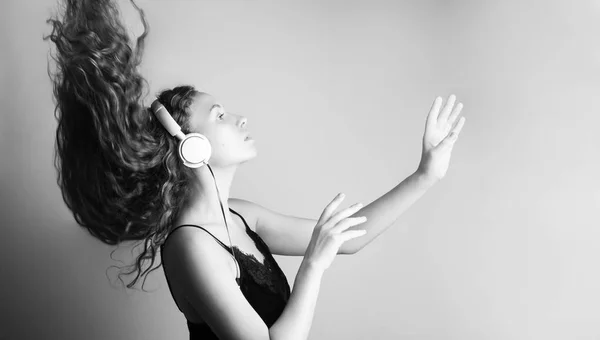 白い壁の前にヘッドフォンで音楽を聴く若い美人の黒と白のショット — ストック写真