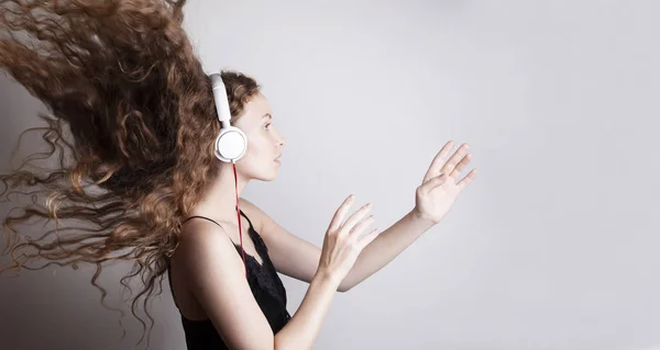 美しい若い女性が白い壁の前にヘッドフォンで音楽を聴く — ストック写真