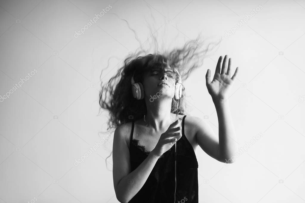 black and white shot of beautiful young woman listening music with headphones in front of white wall and dancing