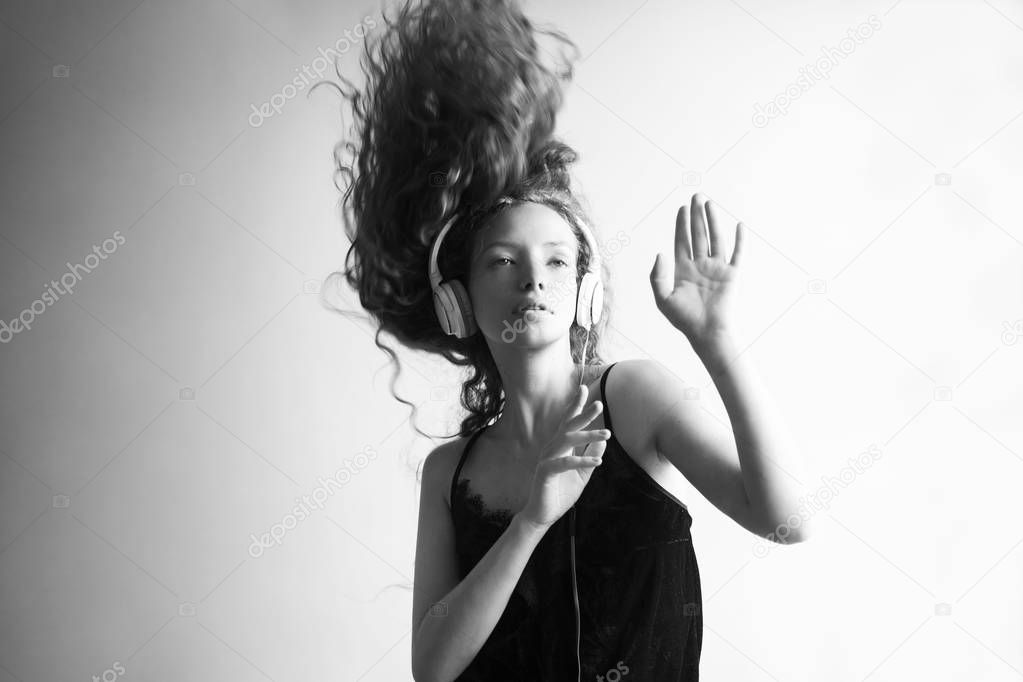 black and white shot of beautiful young woman listening music with headphones in front of white wall and dancing