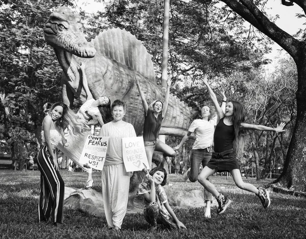 Asian woman in the park next to a dinosaur with a poster \