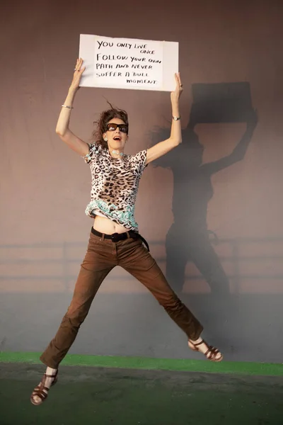 Woman Wearing Eyes Glasses Holding Placard While Jumping Outdoors Building — Stock Photo, Image