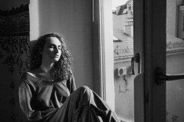 Kıvırcık saçlı güzel kadın pencere eşiğinde oturuyor.