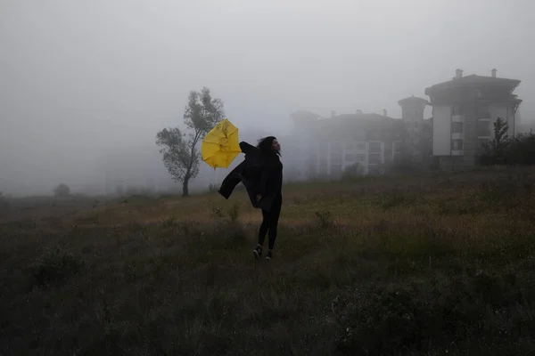 穿着黑色夹克的寂寞女人带着黄色的雨伞在森林的雾中走着 — 图库照片
