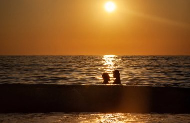 Gün batımı silueti plajda birbirine aşık genç bir çiftin kucaklaşması.
