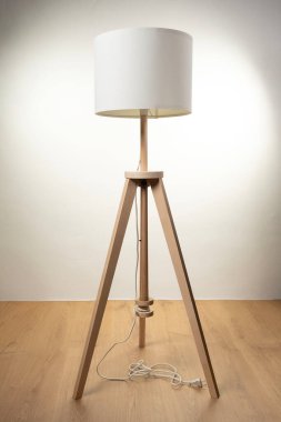 Ahşap tripodlu, beyaz abajurlu, sade ve zarif iç dekorasyonlu süslemeli bir lambanın ön görüntüsü..