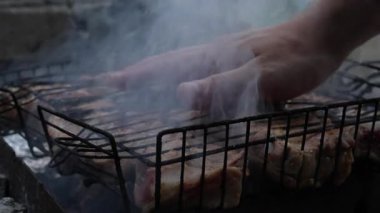 Erkek el testinin 4K 'lık videosunu domuz pirzolasıyla ızgara ızgarasının üstünde kapat. Açık hava yemekleri, piknik ve yemek hazırlama kavramı