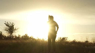Gün batımında çayırda dans eden genç bir kadının 4K videosu. Parlak gökyüzüne karşı siluet özgürlüğü, neşeyi ve doğayla uyumu simgeliyor.