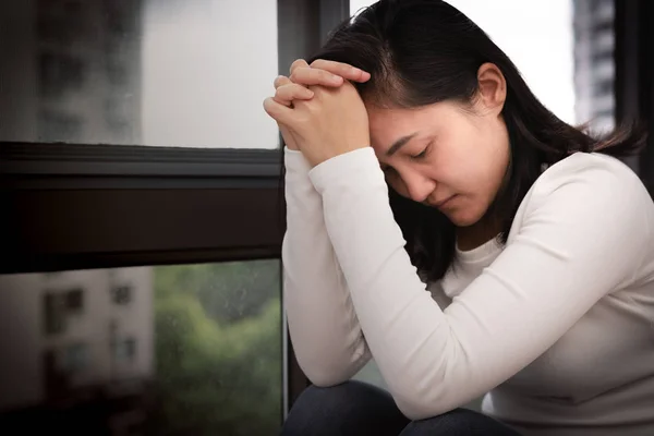 depressed women sitting near window and praying, alone, sadness, emotional concept
