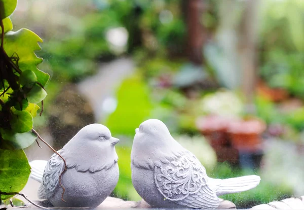 Couple birds, two white bird statues in garden through the window
