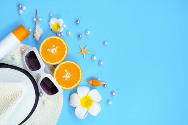 Güzel yaz tatili, plaj aksesuarları, güneş gözlükleri, şapka, turuncu, güneş kremi ve mavi arka planda deniz kabukları.