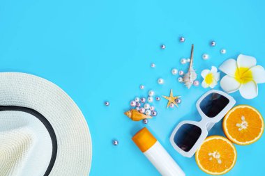 Güzel yaz tatili, plaj aksesuarları, güneş gözlükleri, şapka, turuncu, güneş kremi ve mavi arka planda deniz kabukları.