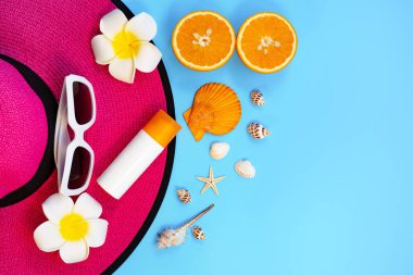 Güzel yaz tatili, plaj aksesuarları, güneş gözlükleri, şapka, turuncu, güneş kremi ve mavi arka planda deniz kabukları.