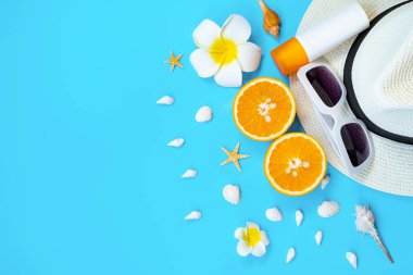 Güzel yaz tatili, plaj aksesuarları, güneş gözlükleri, şapka, turuncu, güneş kremi ve mavi arka planda deniz kabukları.