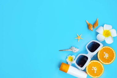 Güzel bir yaz tatili, plaj aksesuarları, turuncu, deniz kabuğu ve mavi arka planda güneş kremi.