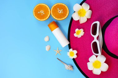 Güzel yaz tatili, plaj aksesuarları, güneş gözlükleri, şapka, turuncu, güneş kremi ve mavi arka planda deniz kabukları.