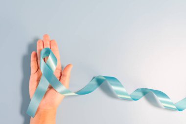 Prostat kanseri farkındalık kampanyası konsepti, erkek sağlığı konsepti. Mavi arka planda açık mavi kurdele uzun kuyruk tutuyor. Kanserle yaşayan erkekler için sembol