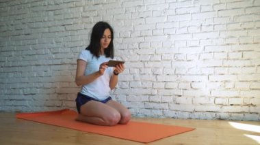 Yoga Mat spor salonunda oturuyor ve seyir telefon kadın.