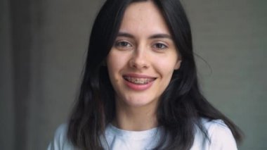 Dişlerini üzerinde parantez genç bir kızla kafasını yatırır ve çerçevede görüntülenir. Beyaz duvar arka planda parantez ile gülümseyen genç kadın