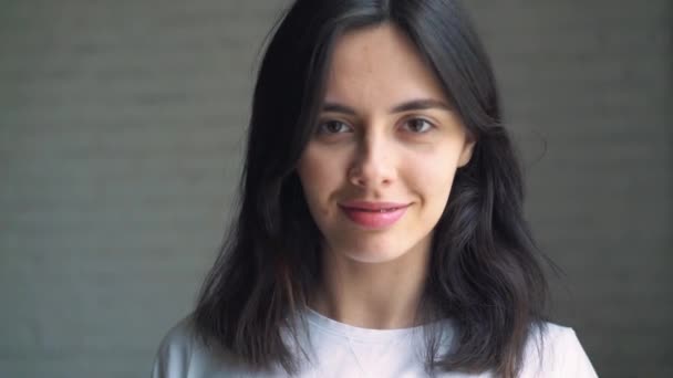 Une jeune fille avec un appareil dentaire penche la tête et apparaît dans le cadre. Jeune femme sur fond mural blanc souriant avec bretelles — Video