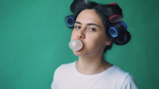 Dívka s natáčky na její hlavu a žvýkačky, vyfukování bublin na zeleném pozadí, chromakey. — Stock video