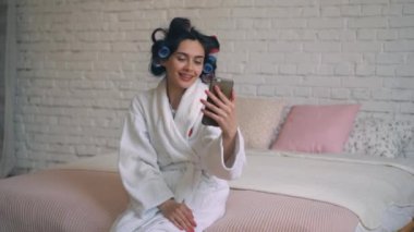 Kız duş curlers ile bornoz oturuyor ve telefonda iletişim kurar sonra.