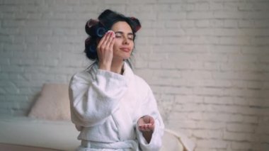 Cilt ile pamuk yastık silerek kıyafeti ve saç curlers içinde yakışıklı tatlı Avrupa kız arkadaşı.