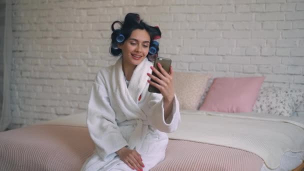 The girl after the shower sits in a Bathrobe with curlers and communicates on the phone. — Stockvideo