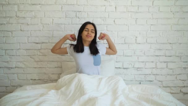 Young attractive woman lying in the bed, enjoying the morning at home. Girl looking at the camera and smiling. — Stock Video